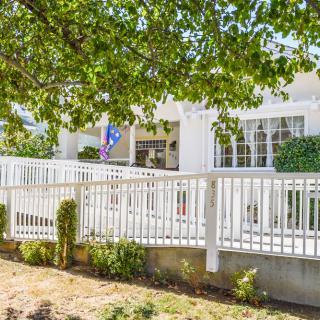 A charming white residential house surrounded by trees, featuring a porch and white fence.
