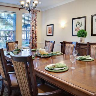 A formal dining room with a large wooden table set for dinner, surrounded by chairs and adorned with tasteful decorations.