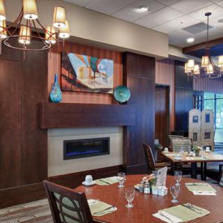 A modern restaurant interior featuring elegant chandeliers, a cozy fireplace, and neatly set tables.