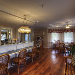 A cozy dining room with elegant chandeliers, wooden flooring, and rattan chairs.