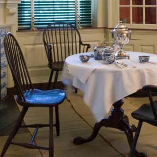 A classic dining room with a round table and chairs, adorned with a silver tea set.