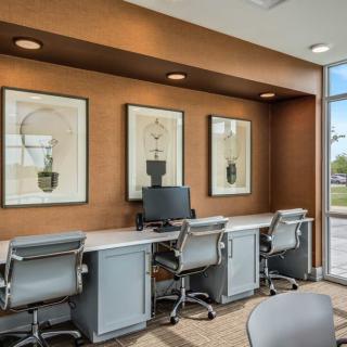 A modern office workspace featuring several desks and chairs, with a computer and framed artwork on the walls.