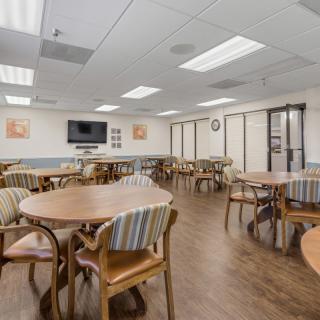 An empty cafeteria with tables and chairs arranged neatly, featuring a television on the wall.