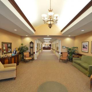 A spacious and elegantly decorated hallway featuring comfortable seating, a chandelier, and framed artwork.