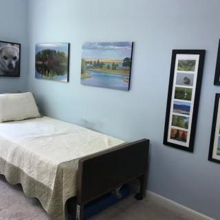 A cozy bedroom with a single bed and various paintings on the walls.