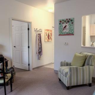 A cozy living room with a striped armchair, decorative artwork, and an open doorway leading to a hallway.