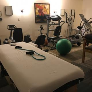 A well-equipped gym area featuring various fitness machines and a treatment table.