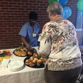 A person serving food to a guest at an indoor event with a buffet setup.