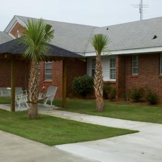 A brick house with palm trees and outdoor furniture on a neatly trimmed lawn.