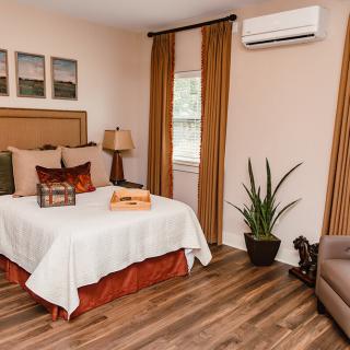A cozy and modern bedroom featuring an air conditioner, wooden flooring, decorative pillows, and a potted plant.