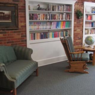 A cozy library corner with bookshelves, a green couch, rocking chair, and a globe.