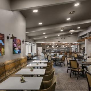 A spacious restaurant dining area with neatly arranged tables and chairs, featuring modern artwork and warm lighting.