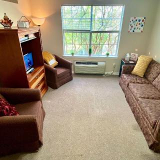 A cozy living room with a sofa, armchair, and a television near a large window.