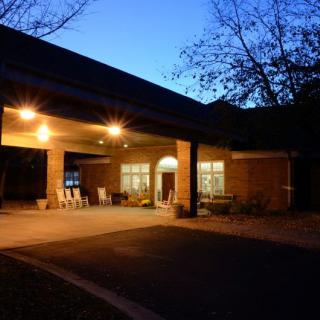 A well-lit building at night with chairs on a covered patio and trees in the background.