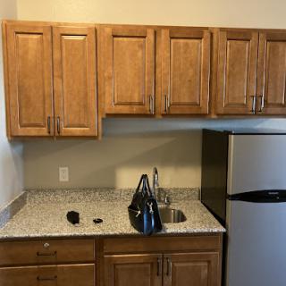 A modern kitchen featuring wooden cabinets, a granite countertop, and a compact refrigerator.