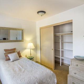 A minimalist bedroom with a single bed, a lamp on a side table, an open closet, and a dresser.