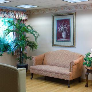 A cozy waiting room with a pink sofa, indoor plants, and a framed painting on the wall.