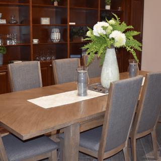 A modern dining room featuring a wooden table with upholstered chairs, adorned with a vase of white flowers.