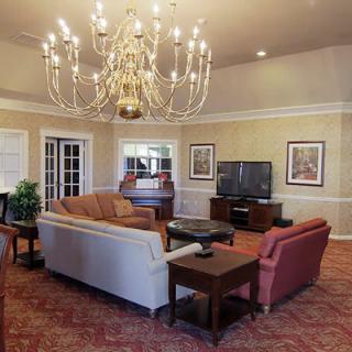 A spacious living room featuring a grand chandelier, comfortable seating, and a large television.
