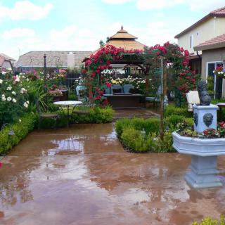 A beautifully landscaped garden featuring a patio, fountain, and vibrant flowers.