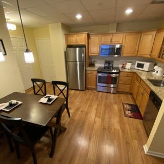A modern kitchen with wooden flooring, featuring a dining table and chairs, stainless steel appliances, and pendant lighting.