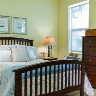 A cozy bedroom with a wooden bed, chest of drawers, and a lamp by the window.