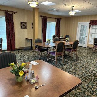A well-furnished dining room with multiple tables and chairs, adorned with floral decorations and warm lighting.