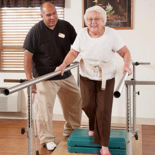 An elderly woman is assisted by a therapist during a physical therapy session.