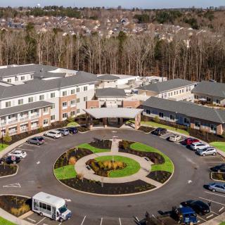Aerial view of a large building with surrounding landscaped areas, parking lot, and vehicles.