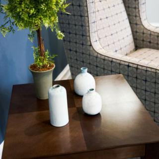 A wooden table with decorative vases and a potted plant next to an upholstered chair.