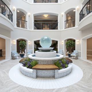 A serene interior atrium featuring a central water fountain surrounded by lush greenery and modern seating arrangements.