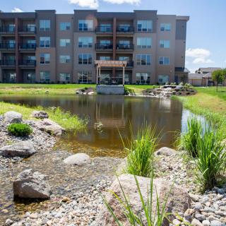An apartment complex with a landscaped pond surrounded by greenery and rocks.