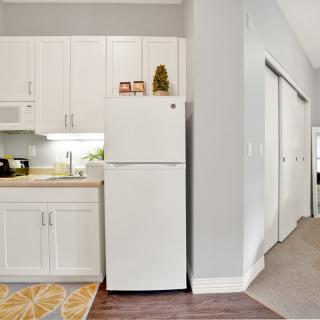 A modern kitchen area in an apartment featuring white cabinets and a refrigerator.