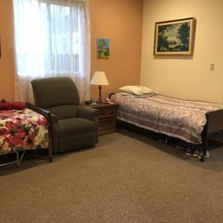 A cozy bedroom with a hospital bed, recliner chair, and decorative paintings.