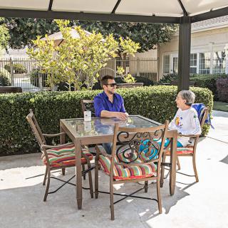 Two people enjoying a conversation at a garden table on a sunny day.