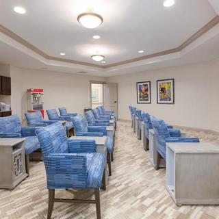 A modern waiting room with blue chairs arranged in rows, illuminated by ceiling lights and adorned with colorful posters on the walls.