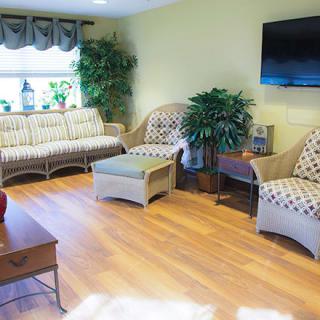 A cozy living room with wicker furniture, a TV on the wall, and decorative plants.