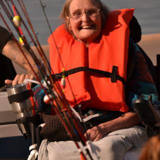 A joyful elderly woman in a life jacket enjoying a fishing trip from her wheelchair.