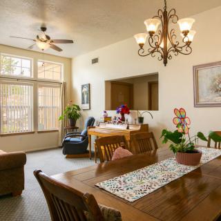 A cozy dining and living area featuring a wooden table, chandelier, and various plants.