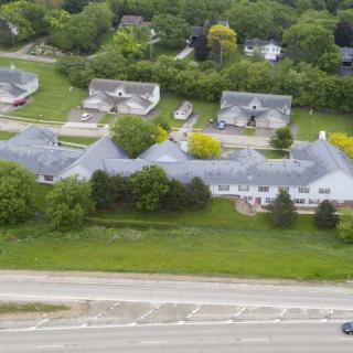 Aerial view of a suburban neighborhood with houses, greenery, and a nearby road.