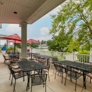 Outdoor patio with tables and red umbrellas, surrounded by greenery.