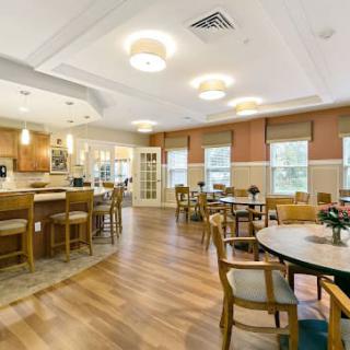 A well-lit dining and kitchen area with wooden flooring and neatly arranged tables and chairs.