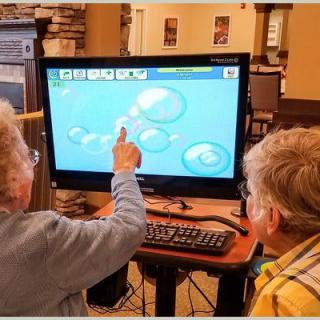 An elderly person and a child interact with an educational program on a computer.