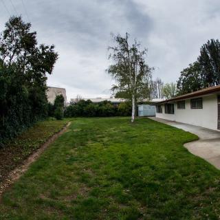 A spacious backyard with a well-maintained lawn, surrounded by trees and adjacent to a house under an overcast sky.