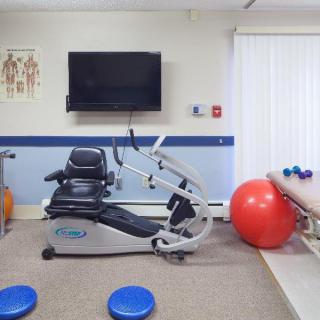 A physical therapy room equipped with a recumbent stationary bike and fitness ball, ready for rehabilitation exercises.