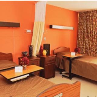 A hospital room with two patient beds and a bright orange wall.