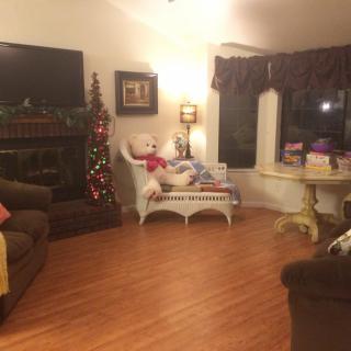 A cozy living room decorated for Christmas with a small tree, teddy bear, and gifts.