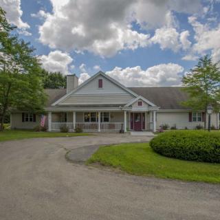 A picturesque residential home with a circular driveway, surrounded by trees under a cloudy sky.