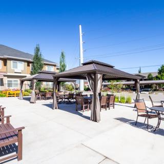 A sunny outdoor patio area with gazebos, chairs, and tables in front of a building.