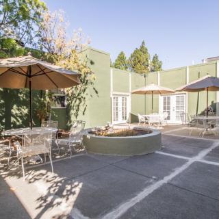 A sunny outdoor patio with tables, chairs, and umbrellas next to a green building.
